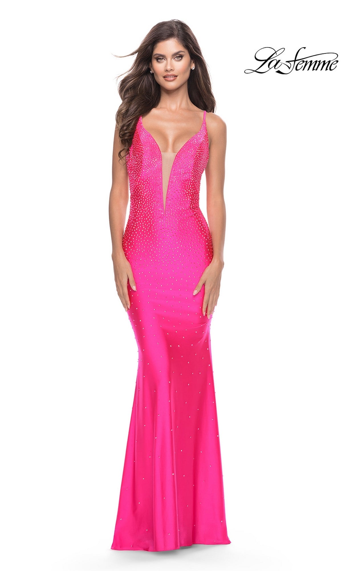 A woman wearing a neon pink, floor-length, fitted jersey Long Prom Dress: La Femme 31413 with a deep V-neckline and a sparkly, embellished bodice.